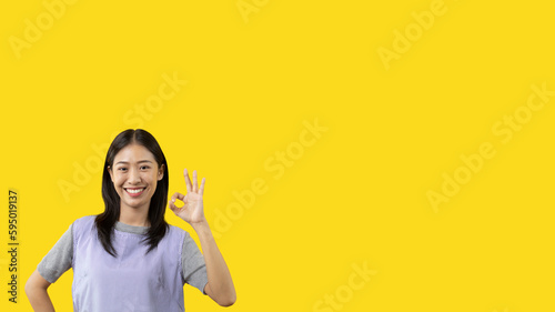 Young asian woman over yellow background doing ok sign with hands, OK symbol, Welcome, Agree, Join, Do as instructed, Follow orders, Acceptance of all conditions.