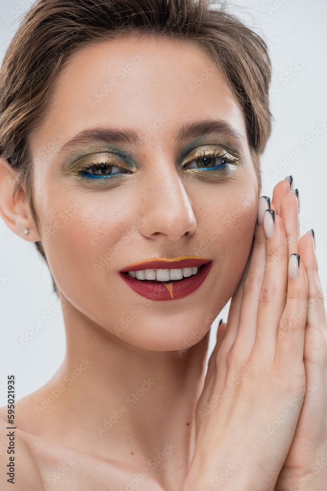 happy young woman with shimmery eye makeup and short hair standing with praying hands isolated on grey.