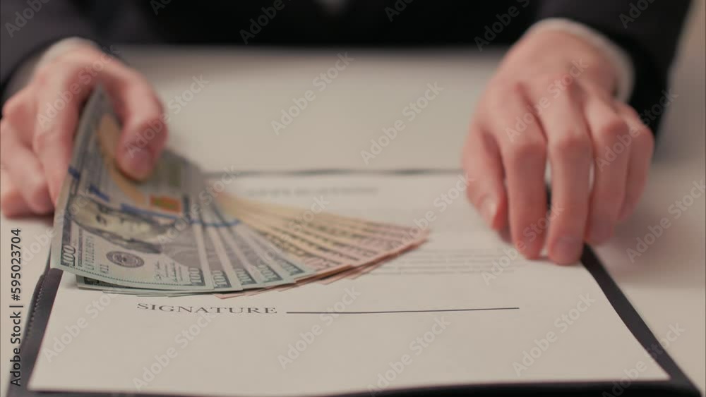 Caucasian Woman Slides Over Contract with Stack of Cash, Pointing at Signature Line. Shot with ARRI Alexa in ARRIRAW at 23.98 fps and exported QuickTime Apple ProRes 422 HQ. Caucasian Woman Slides Over Contract with Stack of Cash, Pointing at Signature Line. Shot with ARRI Alexa in ARRIRAW at 23.98 fps and exported QuickTime Apple ProRes 422 HQ.