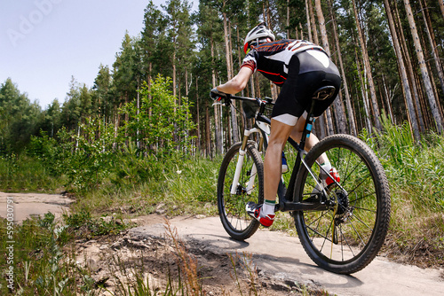 rear view male cyclist riding forest trail on mountainbike, summer cross country cycling race