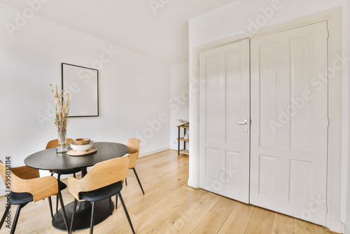 a dining room with white walls and wood flooring the table is surrounded by four chairs in front of the door