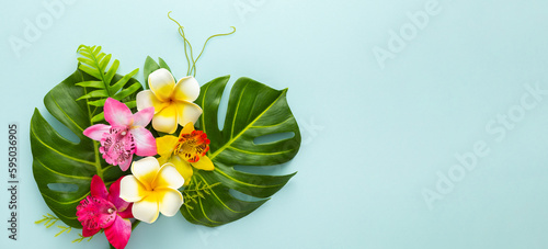 Summer background with tropical orchid flowers and green tropical palm leaves on light background. Flat lay, top view.