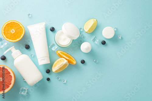 Playful summer skincare concept. Top view flat lay of mock up cream bottles, jars, serum, pipette with juicy citrus fruit slices, flowers on a stylish and fun blue background