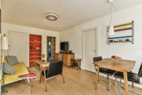 a living room with wood flooring and white walls, there is a small dining table in front of the couch