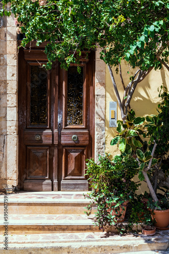 Old shabby wooden door of a Greek house, green tree, stone steps