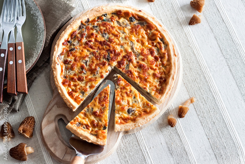 Quiche – open tart pie with morel mushrooms, onion and cheese on wooden cutting board