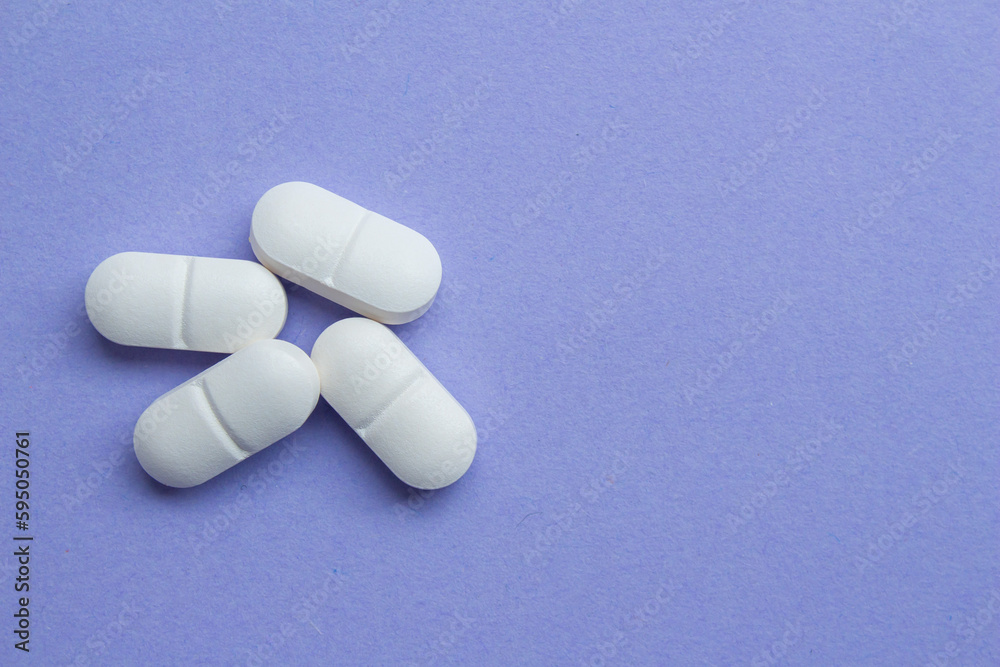 White antibiotic pills isolated on a purple background. White medicines top view, copy space.