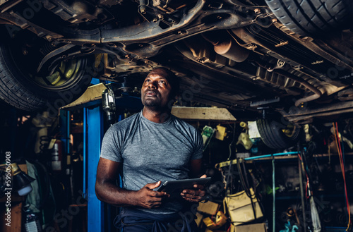 Professional Car Mechanic is Investigating Under a Vehicle on a Lift in Service. Auto Service Worker Checking Car Under Carriage Look For Issues. Car service technician check and repair customer car.