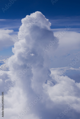 Cumulus and cumulonimbus rain clouds seen from aeroplane. Shot taken in flight against blue sky.