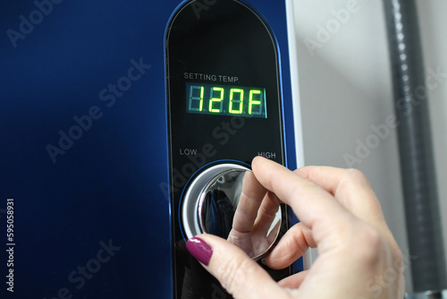 Female hand adjusting a tankless instant hot water heater. Display showing 120°F 