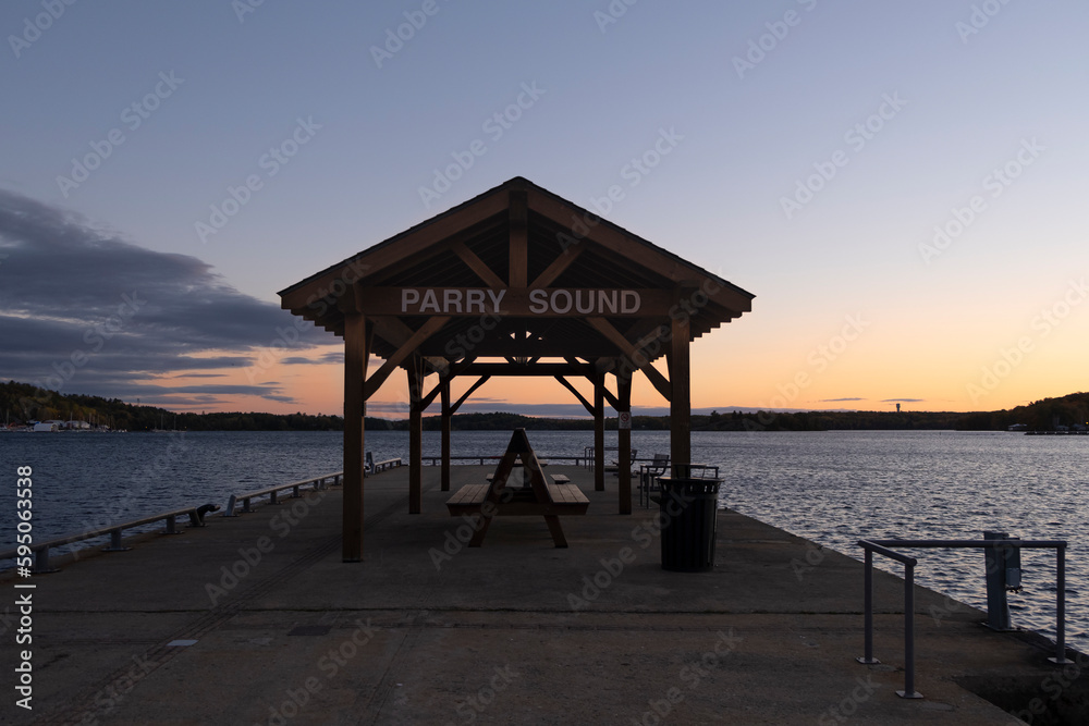 Parry Sound sign on top of covered wooden picnic shelter at the pier facing Georgian Bay at sunset hour.