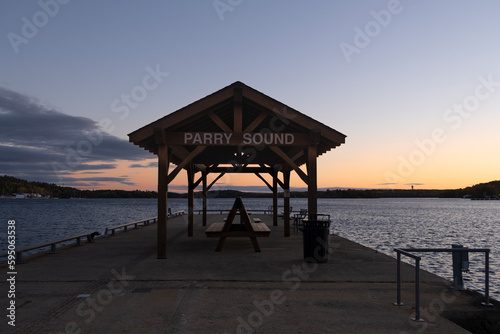 Parry Sound sign on top of covered wooden picnic shelter at the pier facing Georgian Bay at sunset hour.