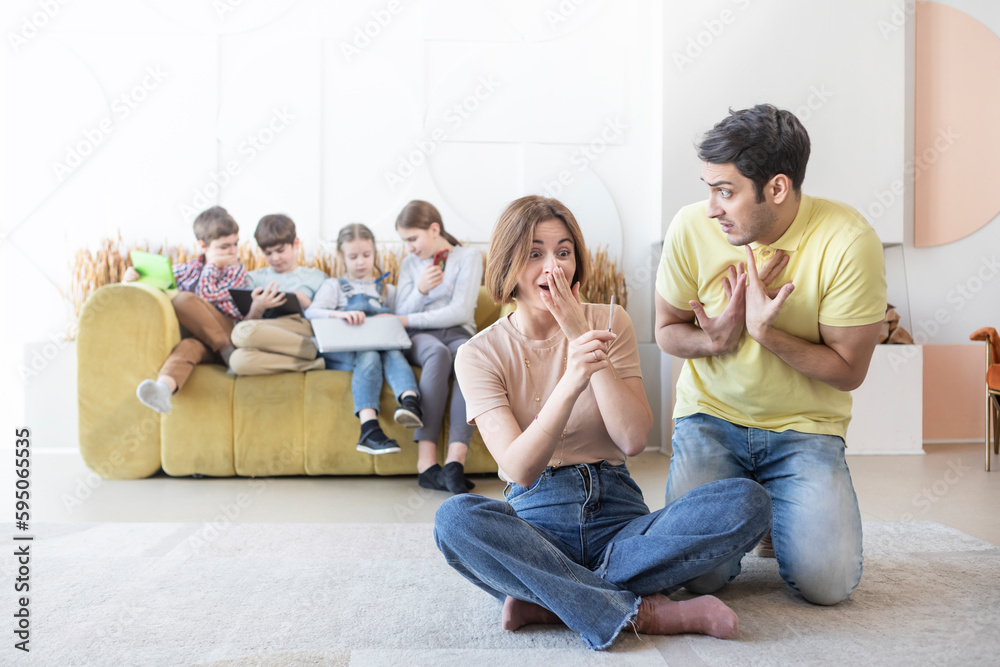 Young Mother of many Children holding pregnancy test and feeling stress because of its positive result and her shocked husband sitting close to her Young Mother of many Children holding pregnancy test and feeling stress because of its positive result and her shocked husband sitting close to her