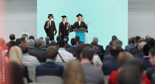 Graduate students of honor and a professor standing on a podium in front of people