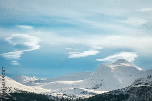 Majestic mountain range blanketed in freshly fallen snow under a blue sky with clouds.