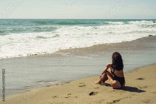 beautiful brunette girl sits on the sand on the beach in front of the sea © sutulastock