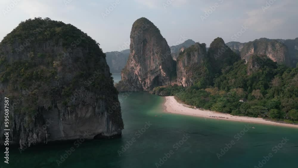 Cinematic aerial view of scenic beach for summer holidays vacation, surrounded by cliffs. Drone video from Thailand, mountains, water and sandy coastline. Popular beach in Krabi, Thailand Railay beach