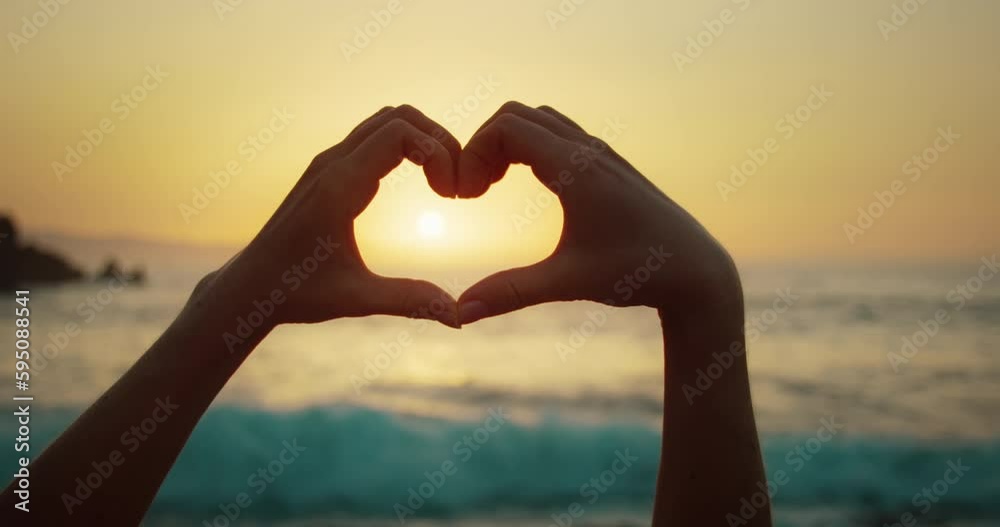 Woman on beach making heart with hands at sunset light on ocean. Sign of love close-up in slow-motion.