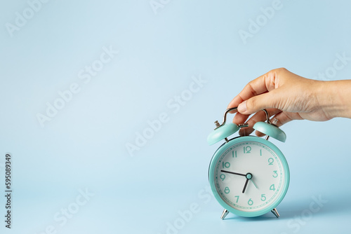 The bell alarm clock is turned off by hand against blue background