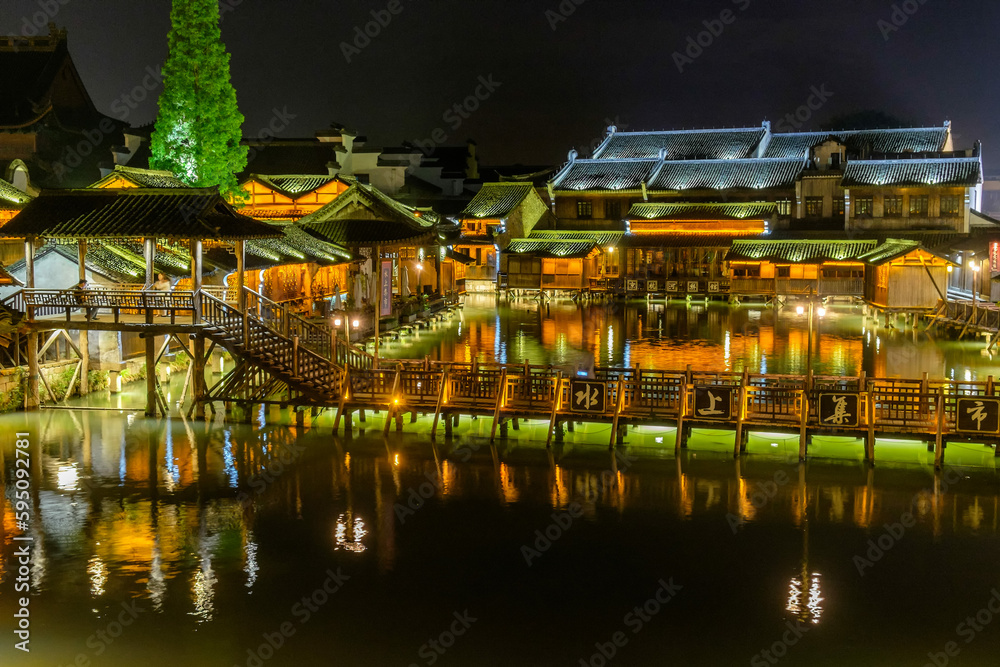 Fototapeta premium Night time view of flat wooden bridge crossing the canal surrounded by traditional Chinese houses in the historic scenic Wuzhen water town, China