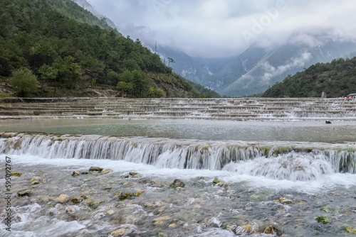 Cascading mini waterfalls of the Baishui River surrounded by the fog covered peaks of Jade Dragon Snow Mountain in Blue Moon Valley  Yunnan  China