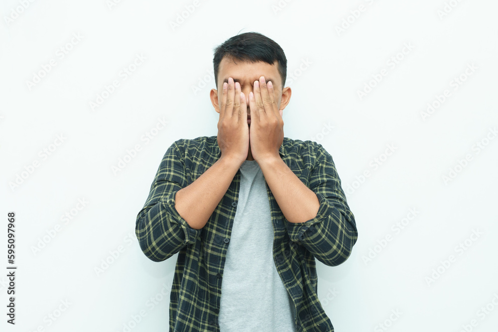 Young Asian man covering his face using hand palms Young Asian man covering his face using hand palms