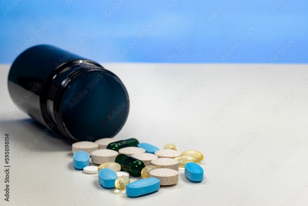 Pill bottle filled with assorted prescription tablets resting alongside a pile of vibrant pills