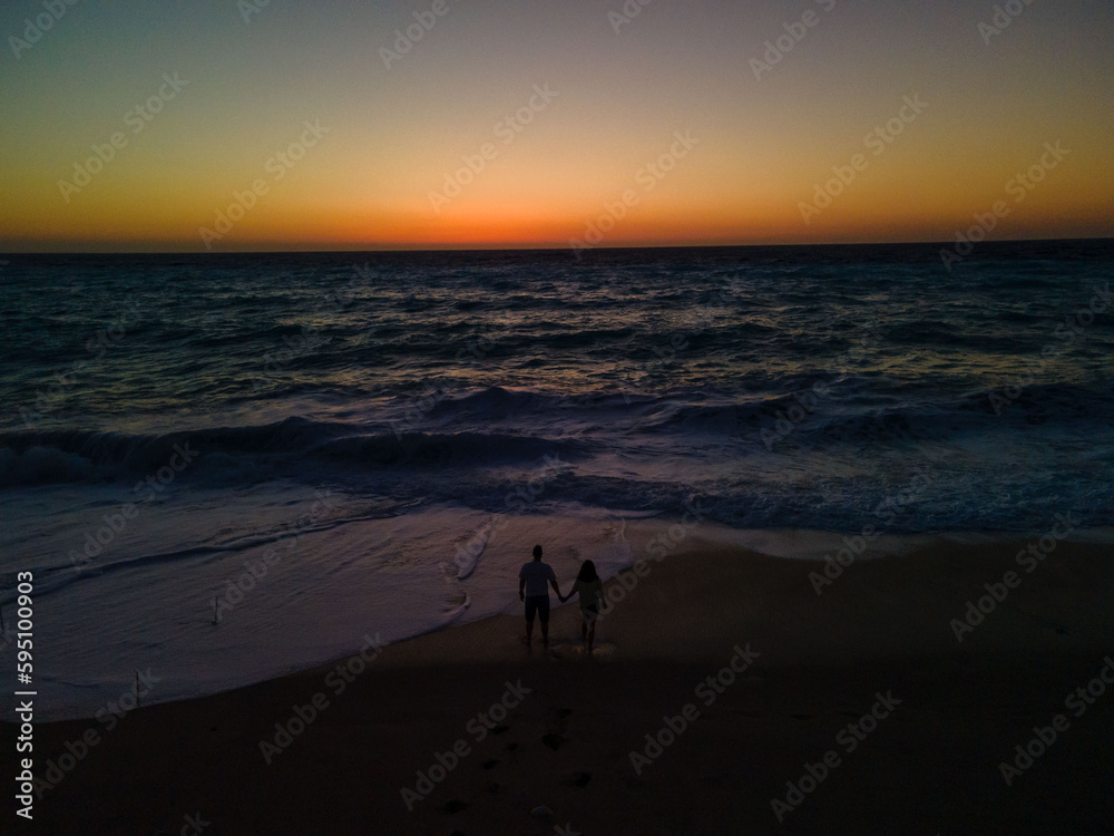 silhouette of couple standing at sea beach looking at strong waves