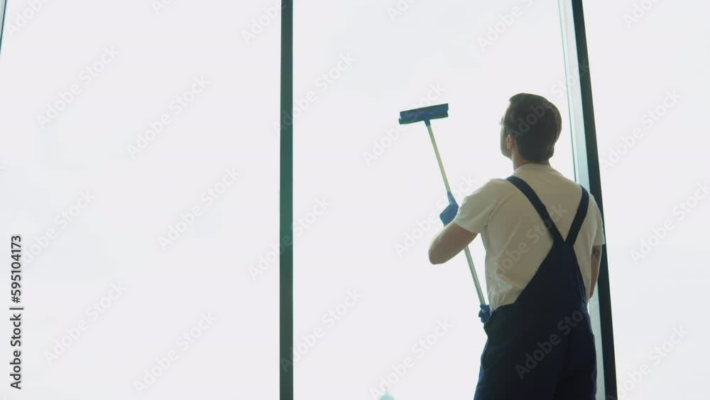Male professional cleaning service worker in overalls cleans the windows in office with special equipment