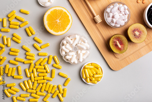 Natural vitamins from fruits and honey and vitamin pills, organic minerals in small bowls from above on wooden desk on light background. Orange, kiwi and honey as sources of natural vitamins.