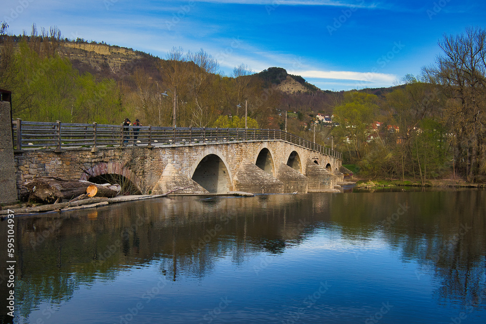 Fototapeta premium Historische Alte Burgauer Brücke über die Saale mit Spiegelung im Wasser unter strahlend blauem Himmel, Jena, Thüringen, Deutschland