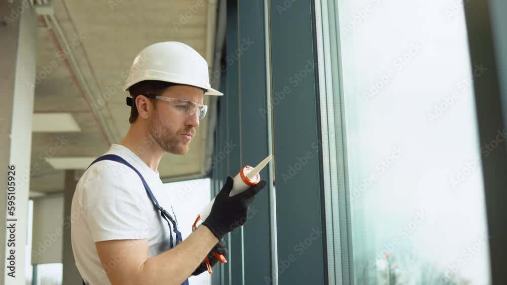 Young worker sealing joints of office window Young worker sealing joints of office window