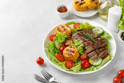 Roast beef salad on white plate and grey background. Salad, meal with meat steak, grilled corn and beef meat with vegetable. Diet dinner concept.