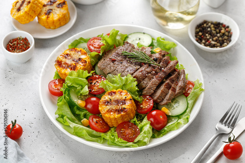 Roast beef salad on white plate and grey background. Salad, meal with meat steak, grilled corn and beef meat with vegetable. Diet dinner concept.