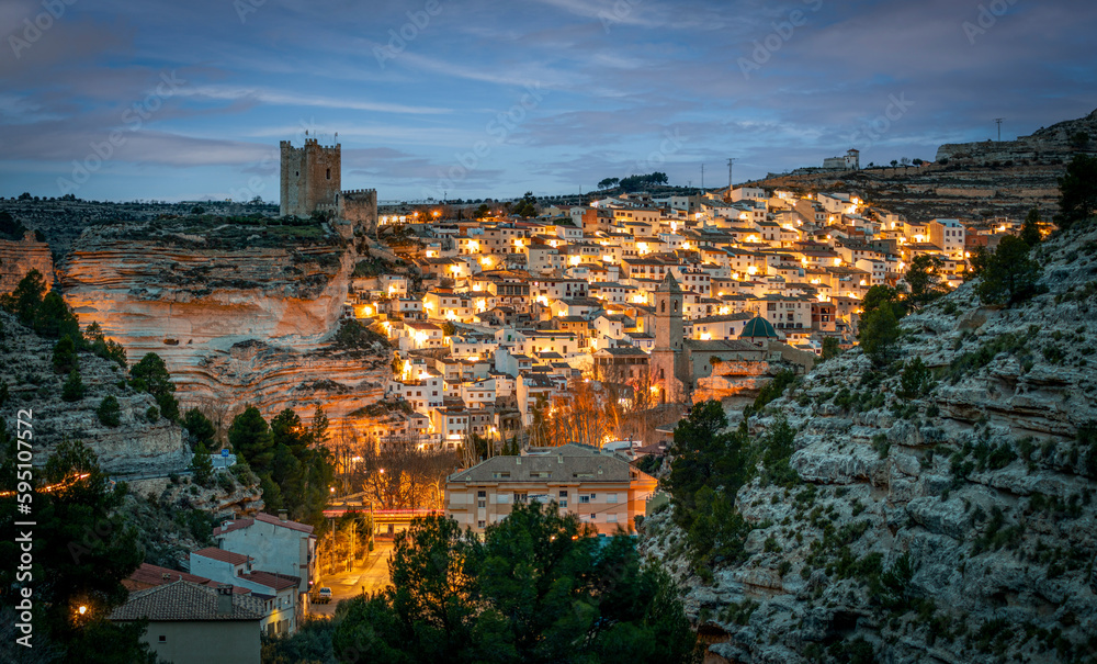 Panoramic view at dawn of Alcalá de Júcar, Albacete, Spain, with illumination of streetlights and castle in the upper part of the town