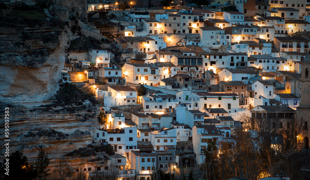 View of part of the old town of Alcala del Jucar in Albacete, Castilla La Mancha, Spain, with the white houses illuminated by streetlights at dawn