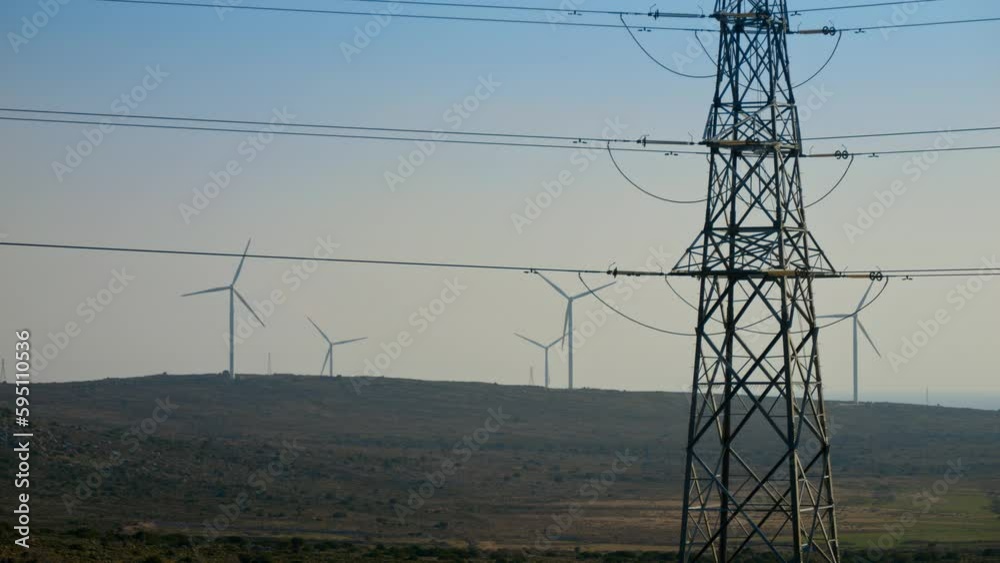 Valley with rotating wind turbines and high voltage power lines ...
