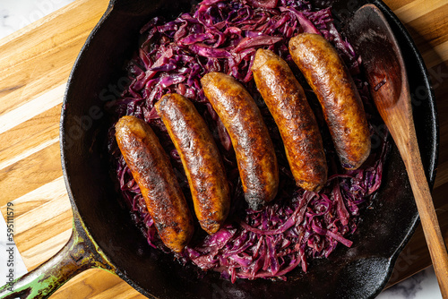 Beer-braised bratwurst sausages with red cabbage and onion in a cast-iron skillet.
