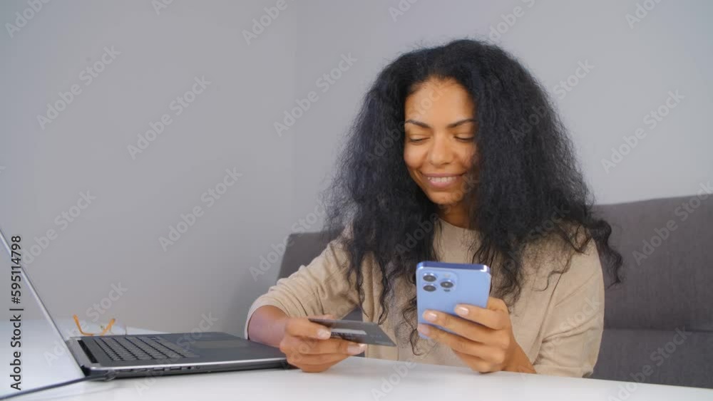 Cheerful black woman making a purchase online with a credit card and mobile phone. Happy customer shopping online with a modern smartphone