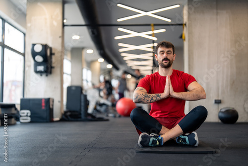 Athletic man in sports clothes with hands clasped practicing Yoga meditation  sitting on exercise mat at health club.