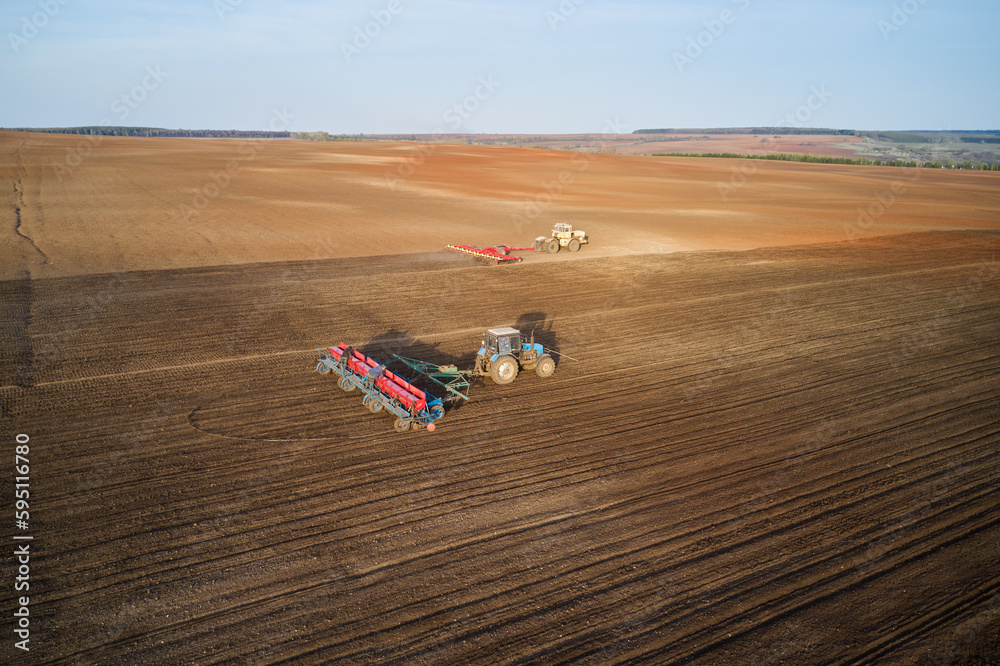 Sowing company. Agricultural machinery in the field: tractor with a seeder in the foreground, in the distance a tractor with a cultivator. Filming from a drone.