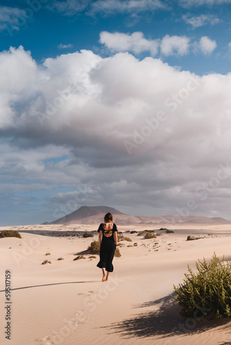 Mujer con vestido andando por el desierto de las dunas de corralejo en Fuerteventura, en verano, durante un viaje vacacional por las islas canarias. photo