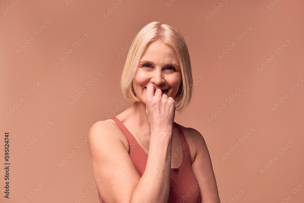 Shy beautiful middle-aged woman on a beige background smiles covering her mouth with her hand. Shy beautiful middle-aged woman on a beige background smiles covering her mouth with her hand.