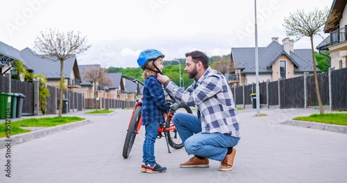 Caucasian father teaching small cute son riding a bike. Dad putting on helmet on head of little boy. Outdoor. Learning how to ride bicycle.