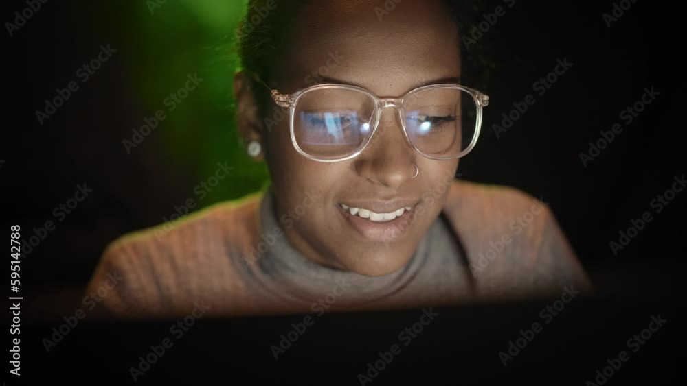 Smiling cheerful mixed race business woman works on computer in dark room. Confident young enterprising girl using laptop computer reading good news on social media. Connected people.