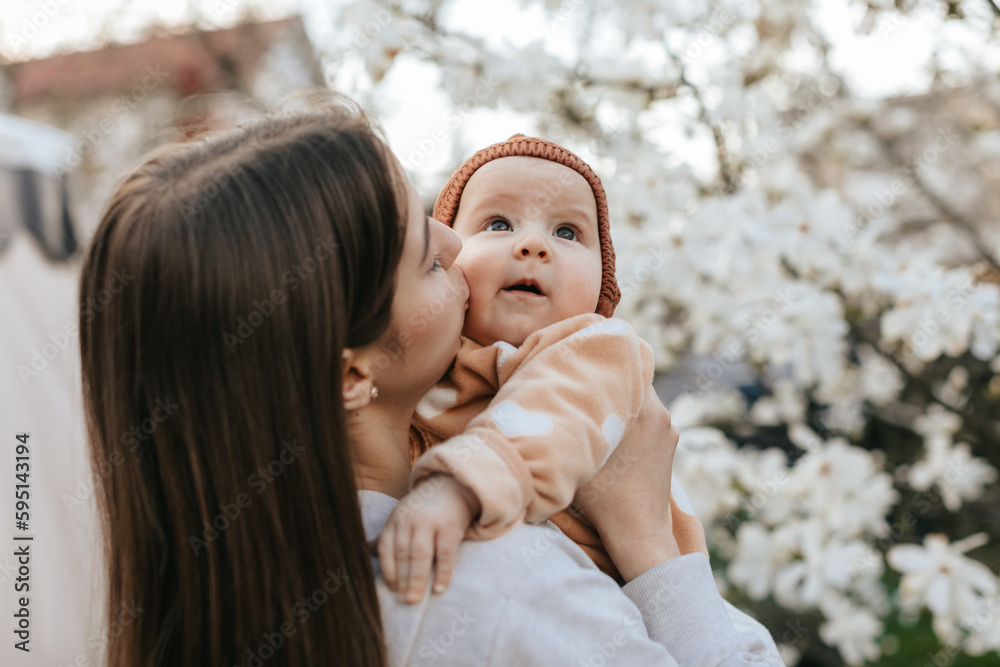 teenage girl with long hair in a grey sweatshirt is holding her newborn sister in a garden with blooming white magnolia. teenage girl with long hair in a grey sweatshirt is holding her newborn sister in a garden with blooming white magnolia.