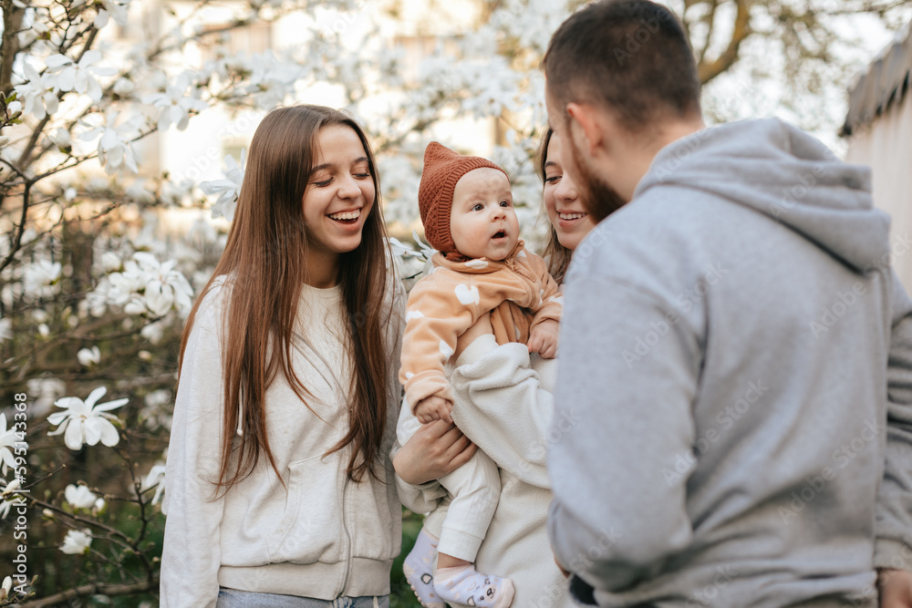 A little baby in the arms of twin sisters was delighted when she saw her father in the blooming garden. Lifestyle. Family concept. Father and Daughter. 