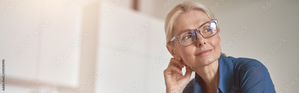 Pensive mature businesswoman looking aside, working from home using laptop computer and drinking coffee in the morning, standing in the kitchen Pensive mature businesswoman looking aside, working from home using laptop computer and drinking coffee in the morning, standing in the kitchen