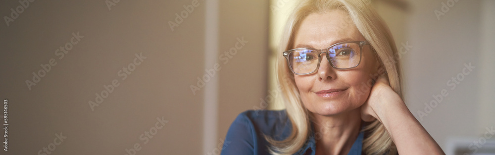 Indoor portrait of attractive mature woman with pleasant smile relaxing on sofa in her modern apartment Indoor portrait of attractive mature woman with pleasant smile relaxing on sofa in her modern apartment