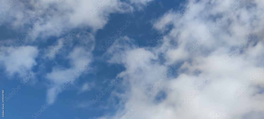 Bright sky above. Spring sunny day, white clouds slowly float in the blue sky. They hang at a low height and they have different shapes and sizes. The clouds are clear and light in spring.